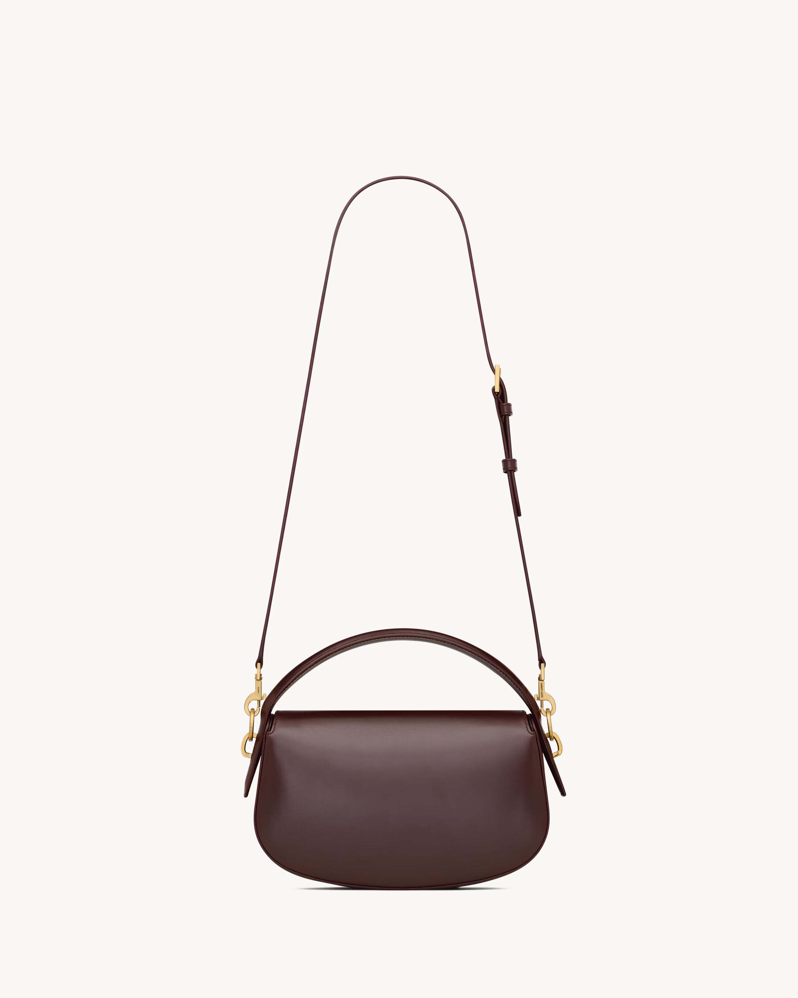 A dark brown Send Saint Laurent  leather crescent-shaped shoulder bag with a top handle, gold-tone hardware, and a long matching shoulder strap, shown against a plain off-white background.